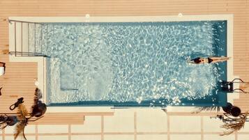 Una piscina rectangular de aguas cristalinas, rodeada por un deck de madera y equipada con una escalera y un trampolín.