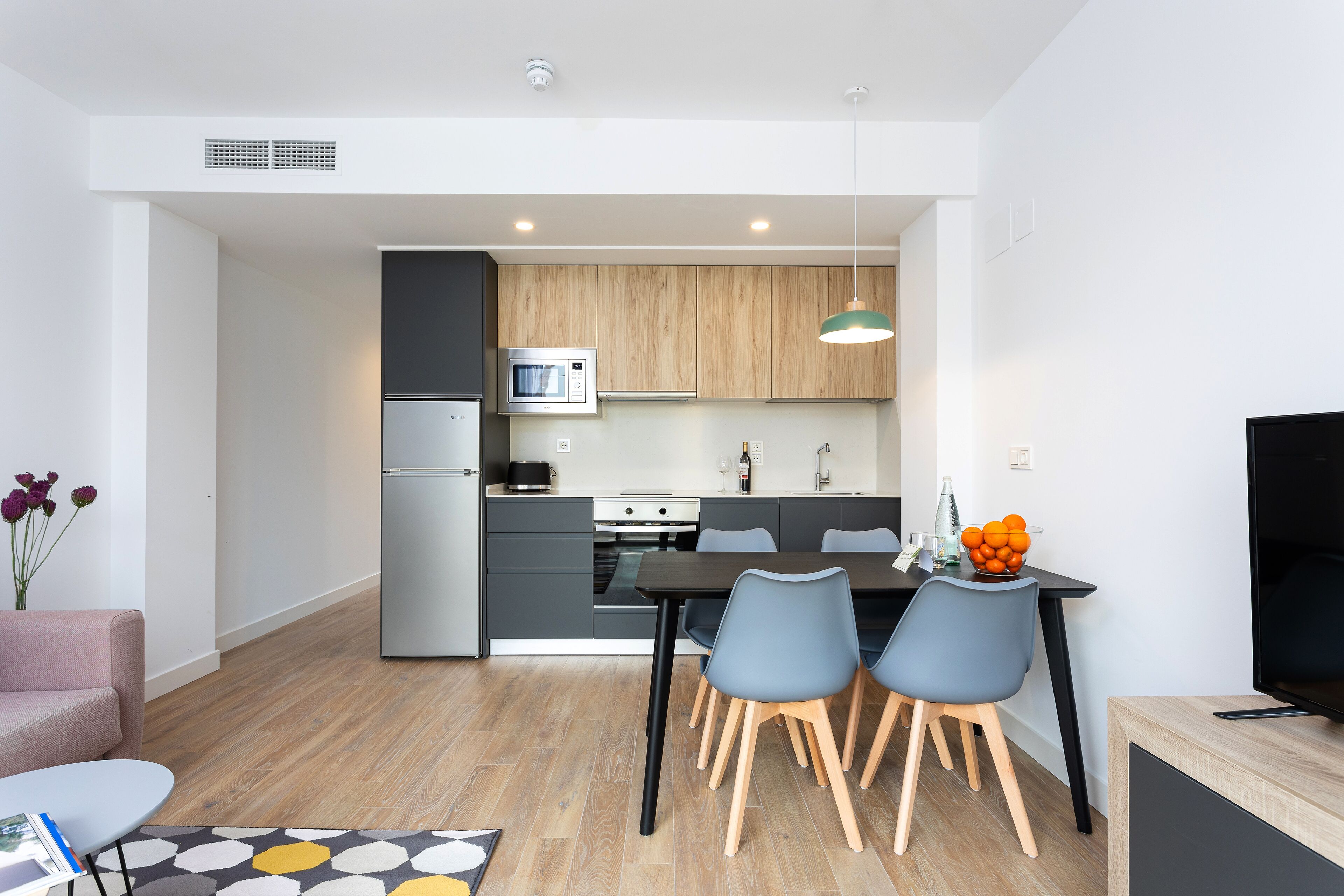 Une cuisine moderne équipée d’un four à micro-ondes, d’un réfrigérateur et d’un coin repas avec des chaises et une table.