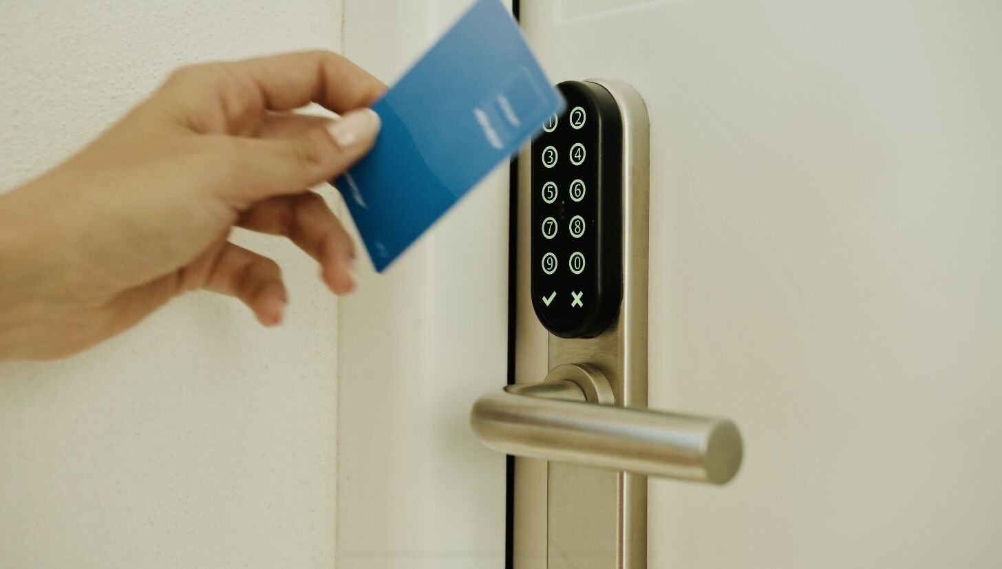 Una mano insertando una tarjeta azul en una cerradura electrónica con teclado numérico.