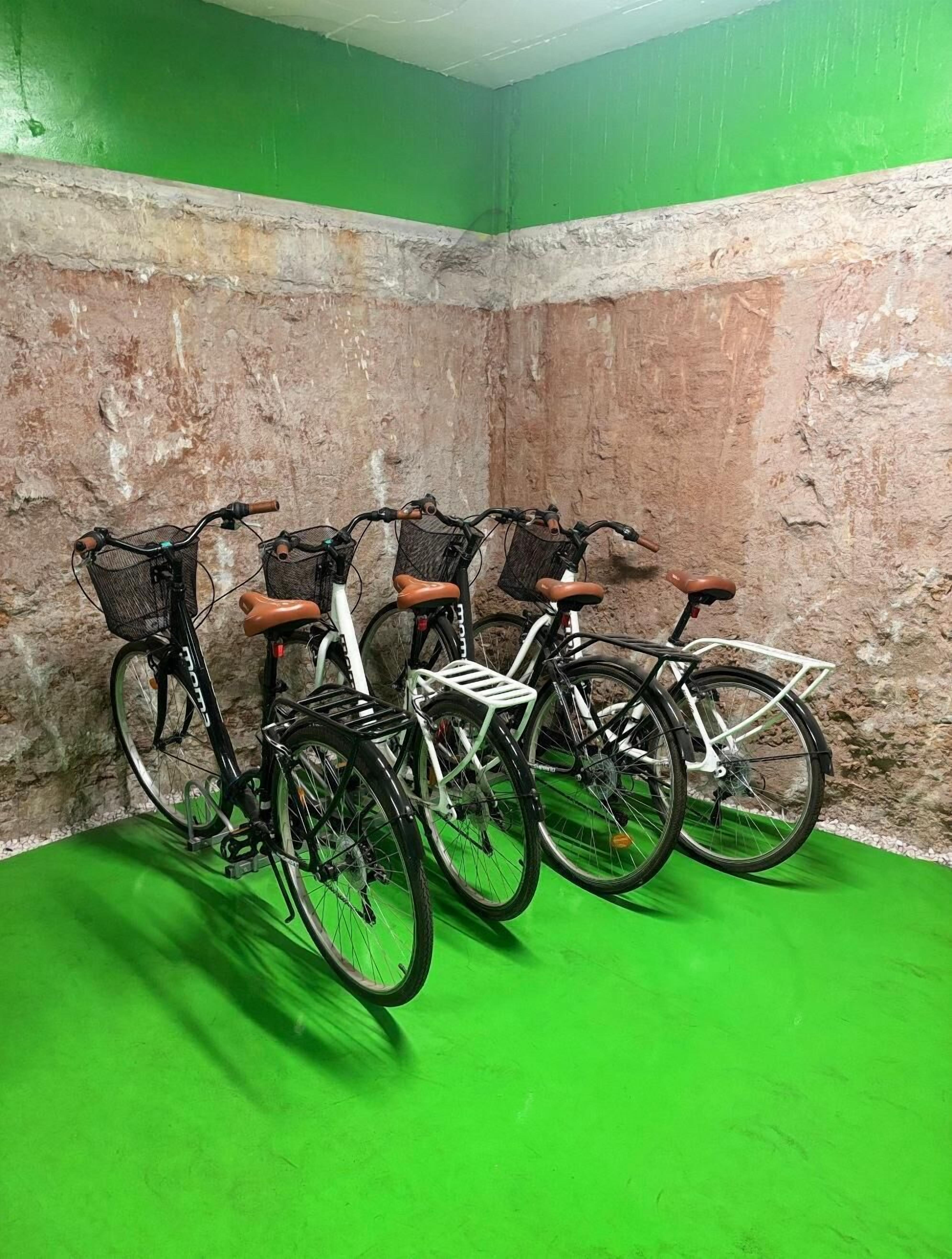Quatro bicicletas estacionadas em frente a uma parede texturizada, chão verde e teto branco.