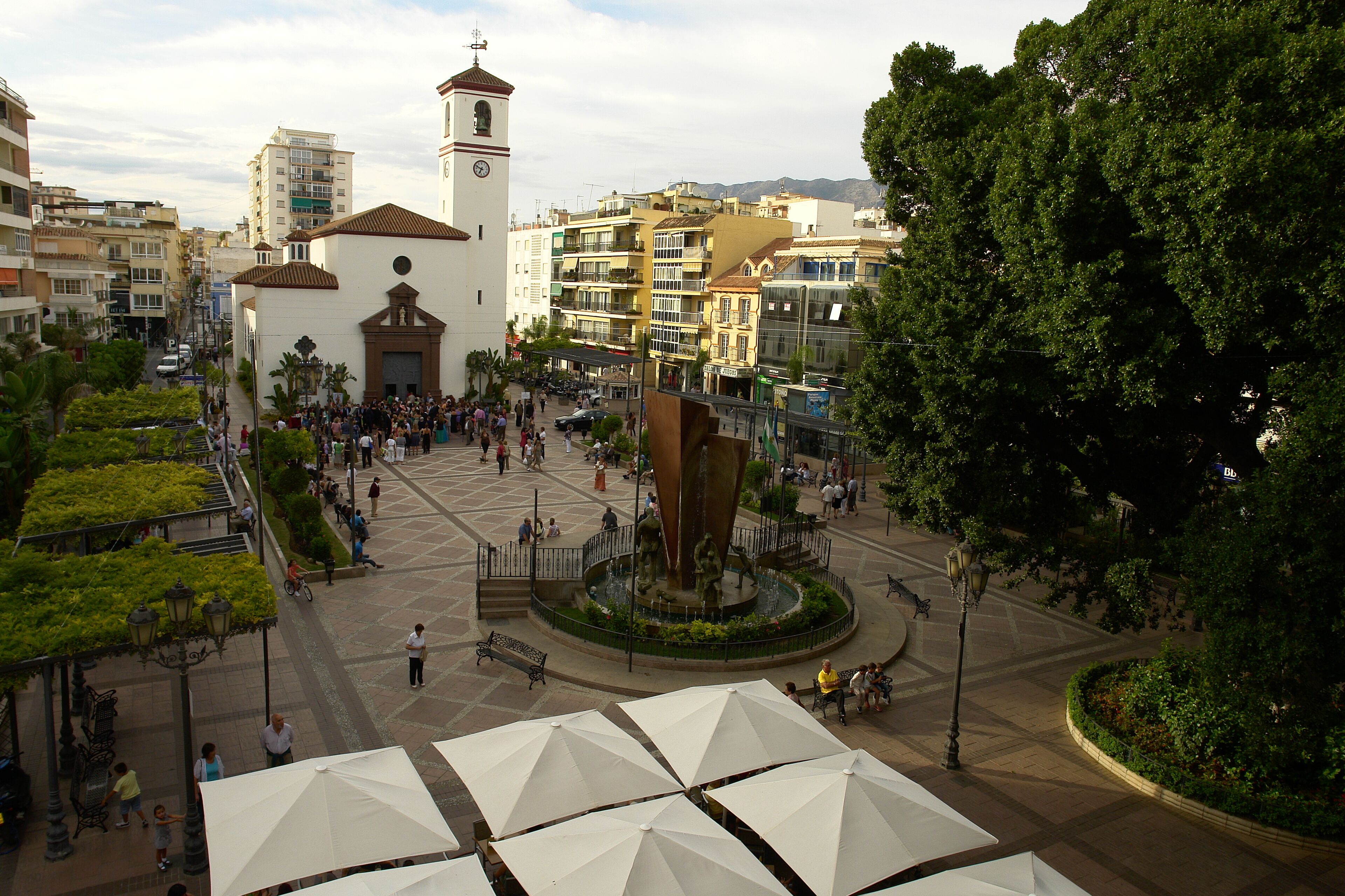 A plaza with a central fountain, surrounded by buildings and trees.