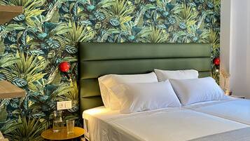 A bedroom with a bed, a nightstand, a lamp, and a wall with a tropical leaf pattern.