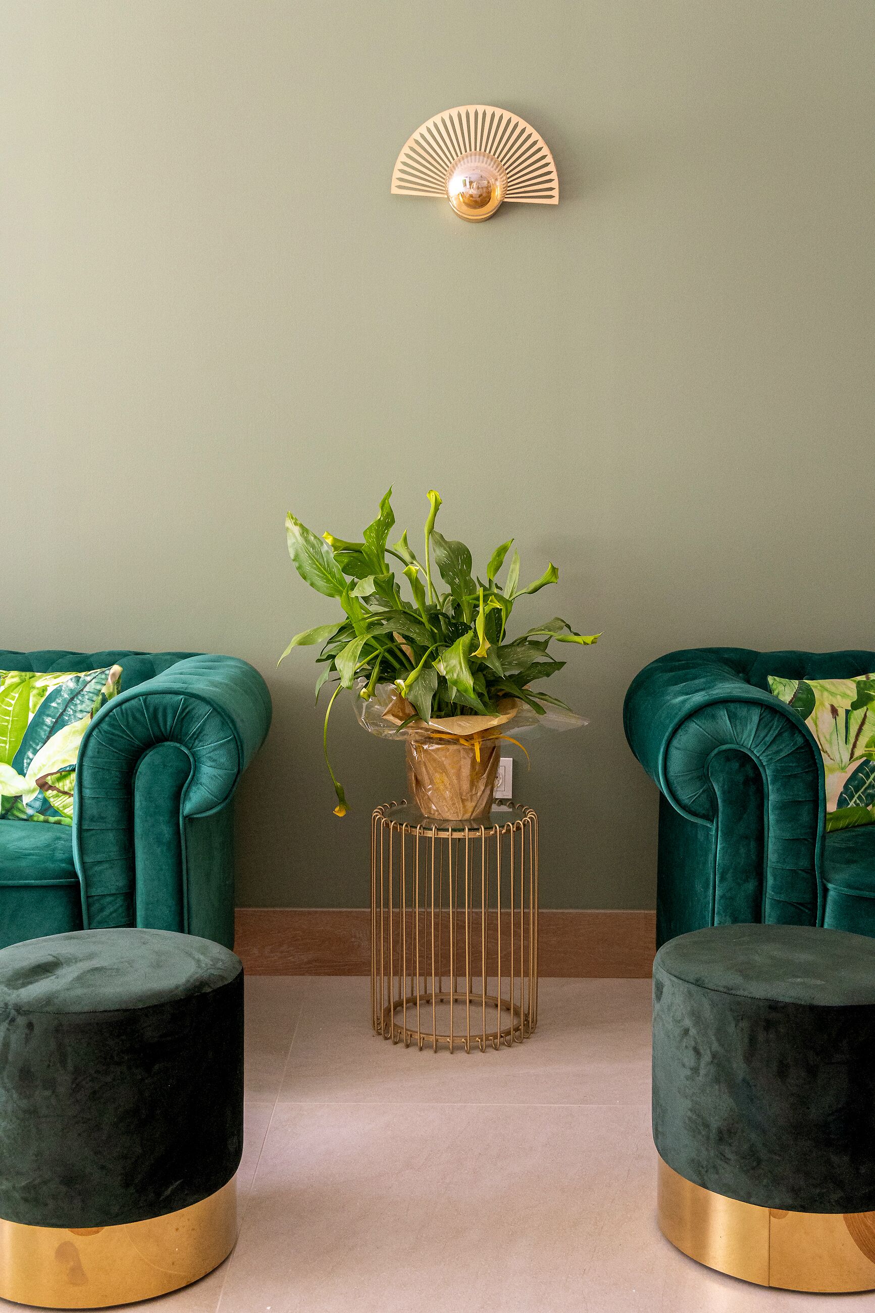 Une pièce comprenant deux canapés en velours turquoise, un petit pouf rond noir avec un pied doré, un radiateur doré et une plante en pot posée sur un support doré.