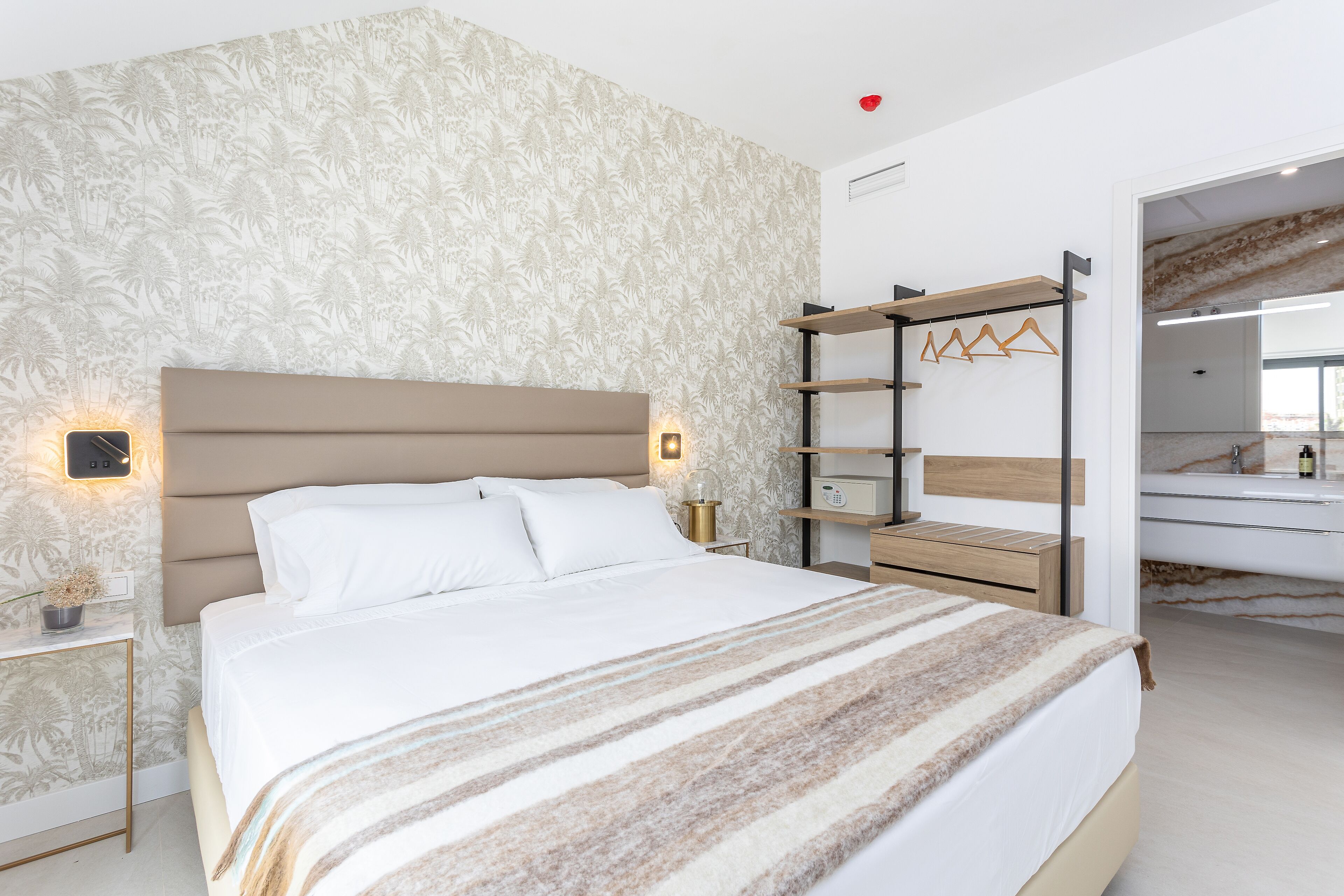A modern bedroom with a large bed, a nightstand, a wall-mounted shelf, and a mirror.