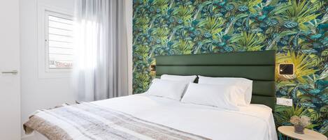 A neatly made bed with a striped blanket, a green headboard, and a tropical leaf-patterned wall.