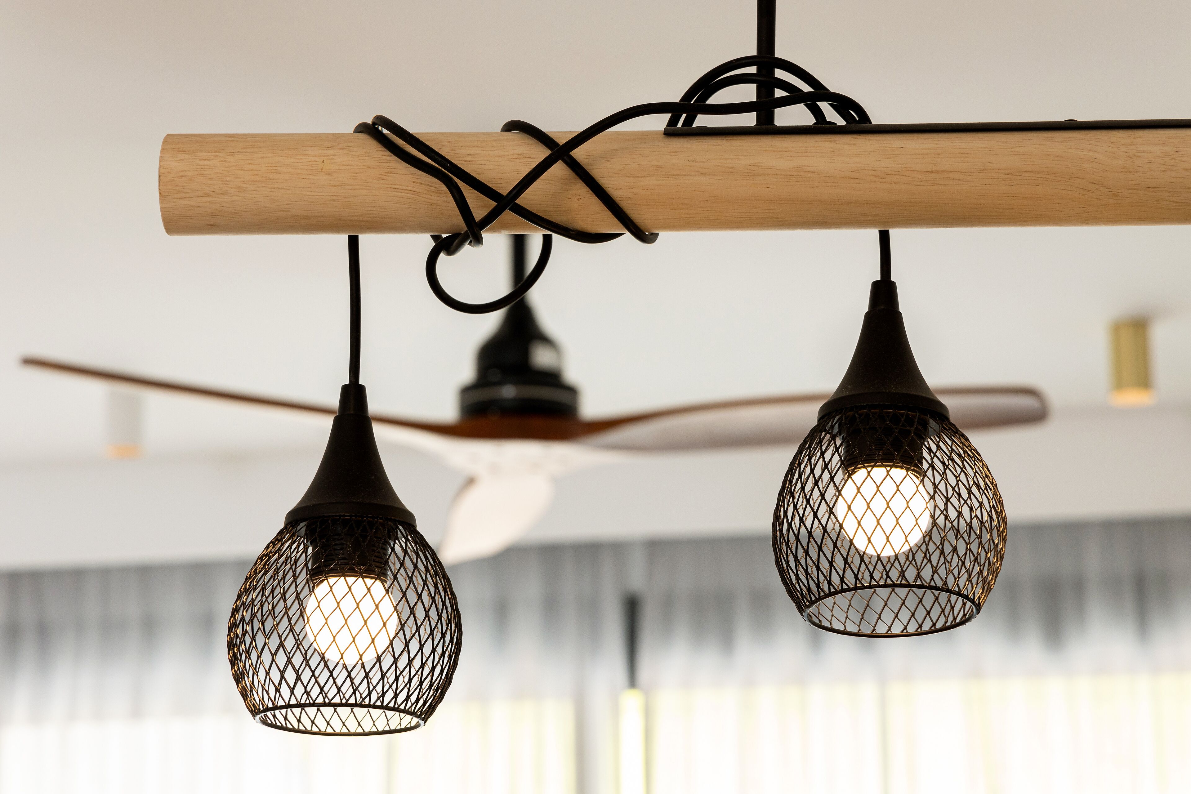 Eine Decke mit zwei hängenden Pendelleuchten im Netzdesign, einem Holzbalken und einem Deckenventilator.