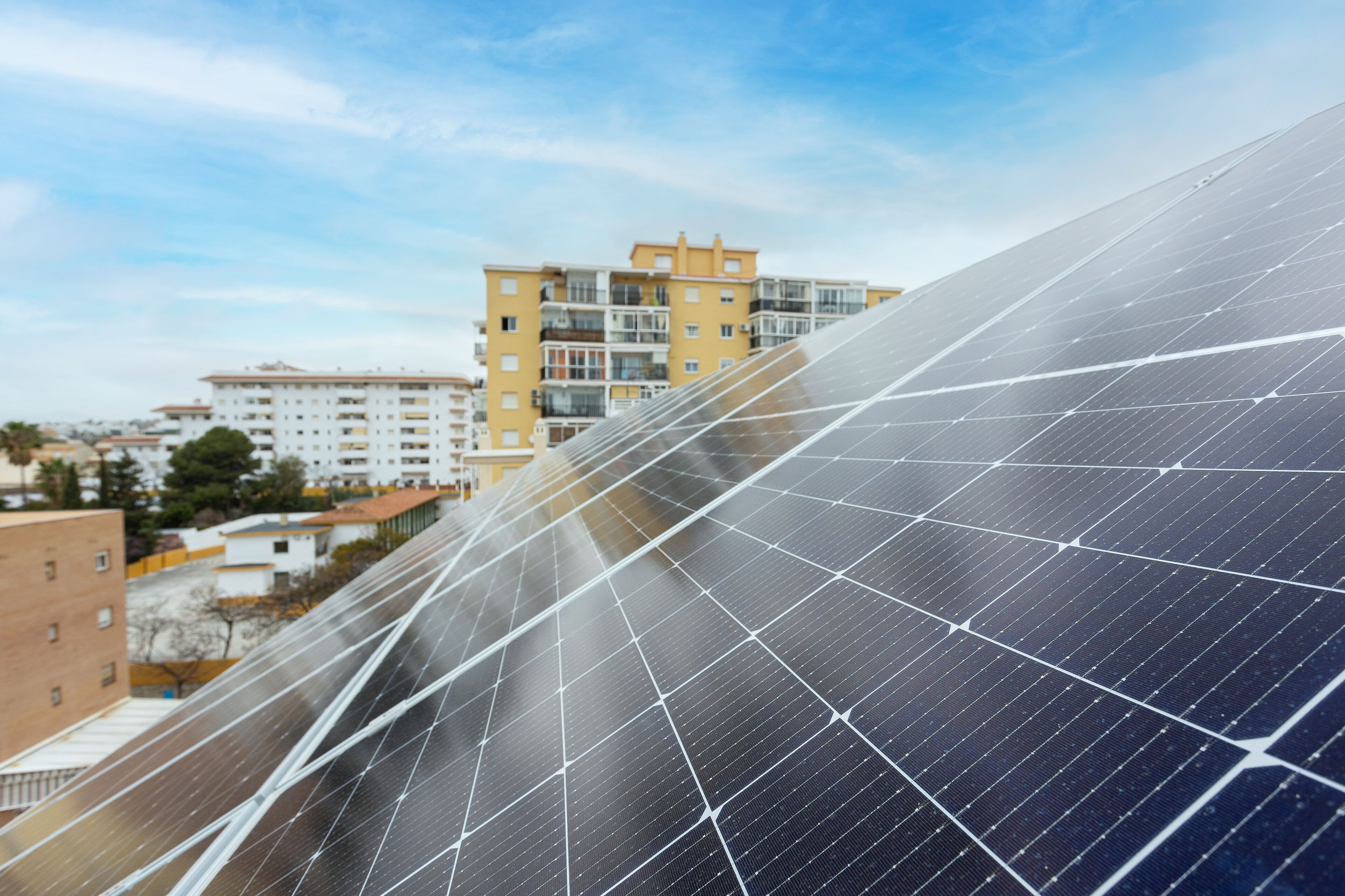 A large solar panel installation with a residential building in the background.