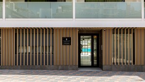 A modern building with a two-story entrance, vertical wooden slats, and a glass door leading to a pool area. - Caleyro Boutique Apartments - Parking incluido (Fuengirola)