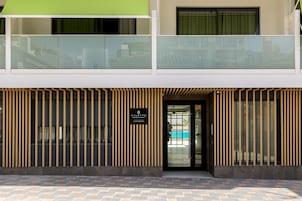 En modern byggnad med en entré i två våningar, vertikala träribbor och en glasdörr som leder till ett poolområde.