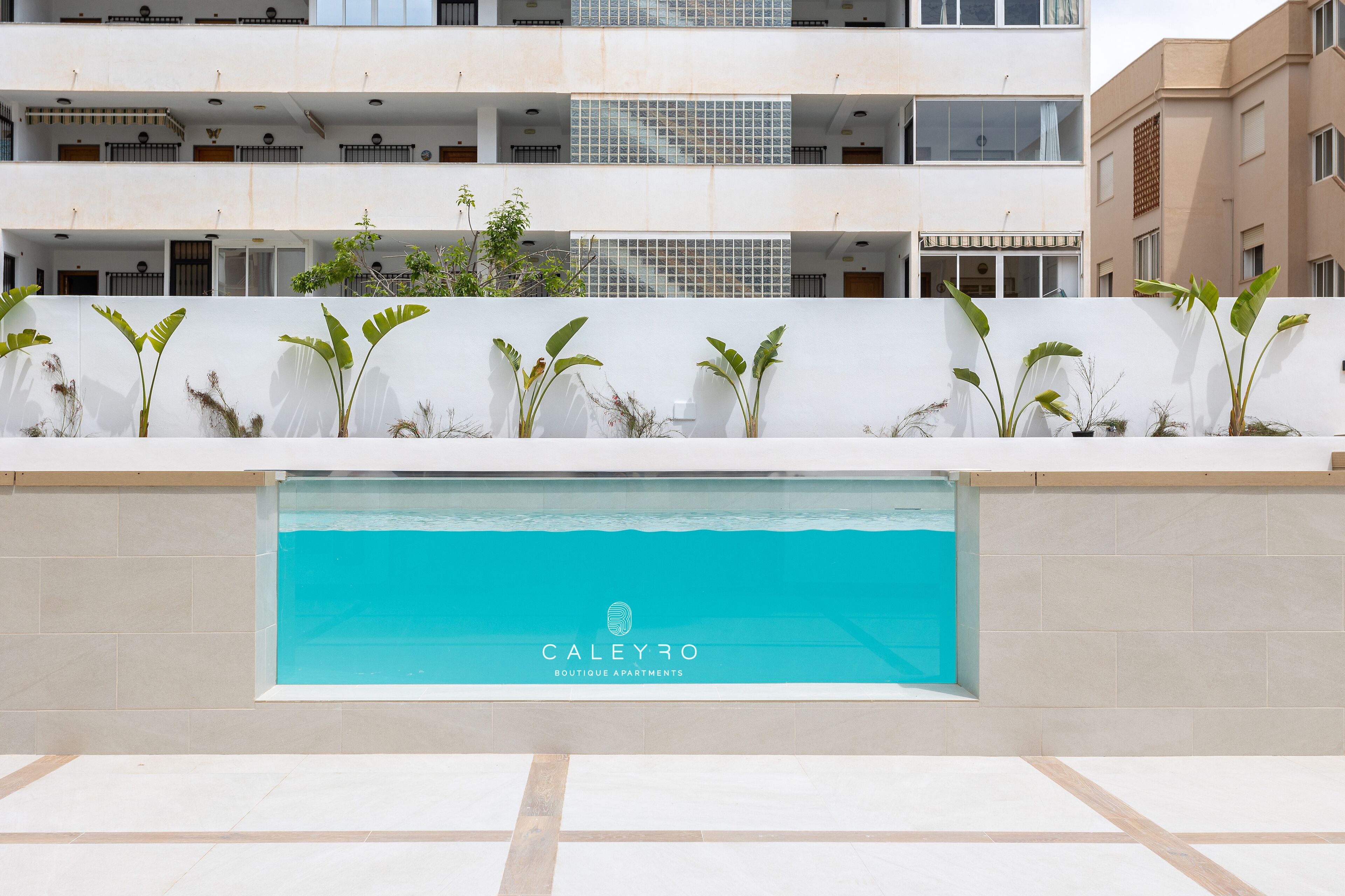 Un moderno edificio de apartamentos con piscina, balcones y plantas en macetas.