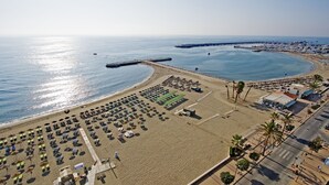 An aerial view of a beach with rows of sunbeds and umbrellas, a pier extending into the sea, and a road alongside the beach. - Caleyro Boutique Apartments - Parking incluido (Fuengirola)