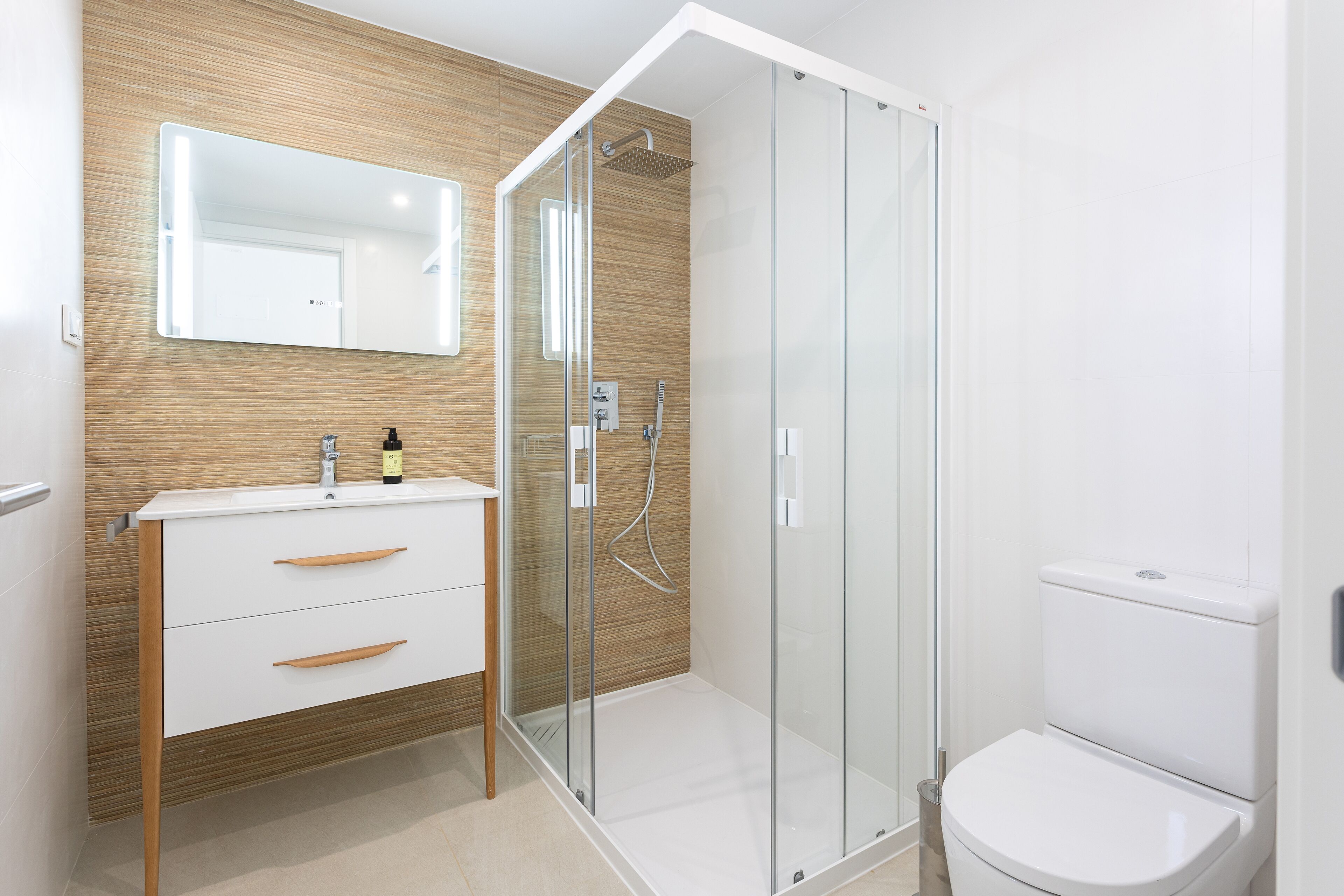 A modern bathroom with a wooden vanity, a glass shower enclosure, and a white toilet.