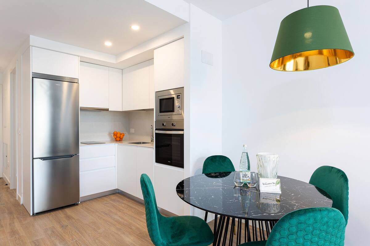 A modern kitchen with white cabinets, stainless steel appliances, and a round table with teal chairs.