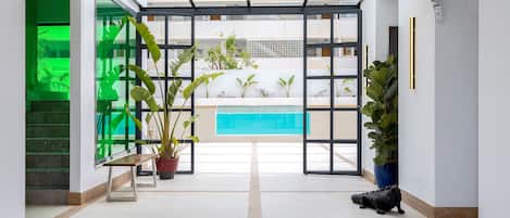 A spacious lobby with a bench, potted plants, and a view of a swimming pool.