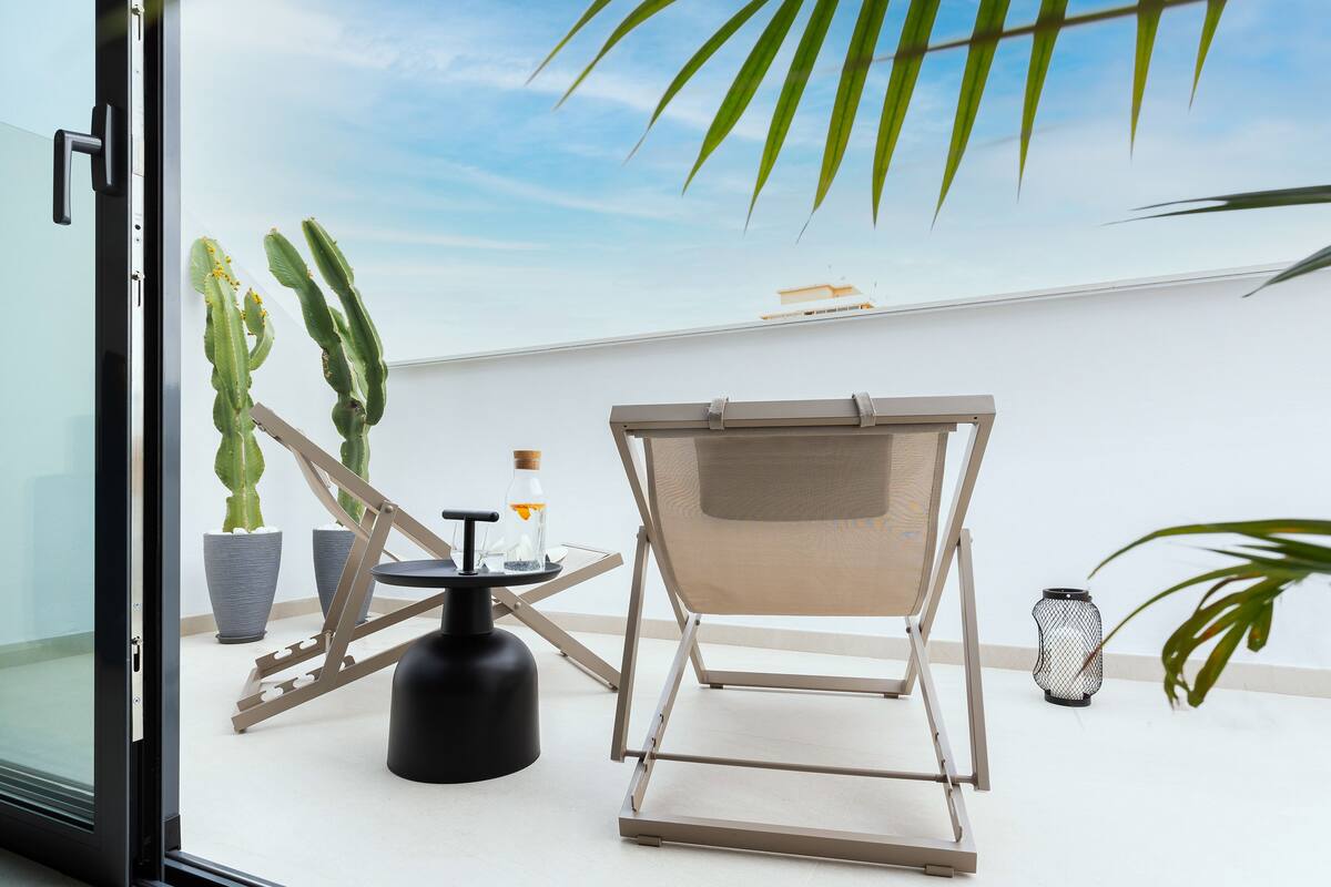 A balcony with a chair, potted plants, a small table, and a decorative lantern.