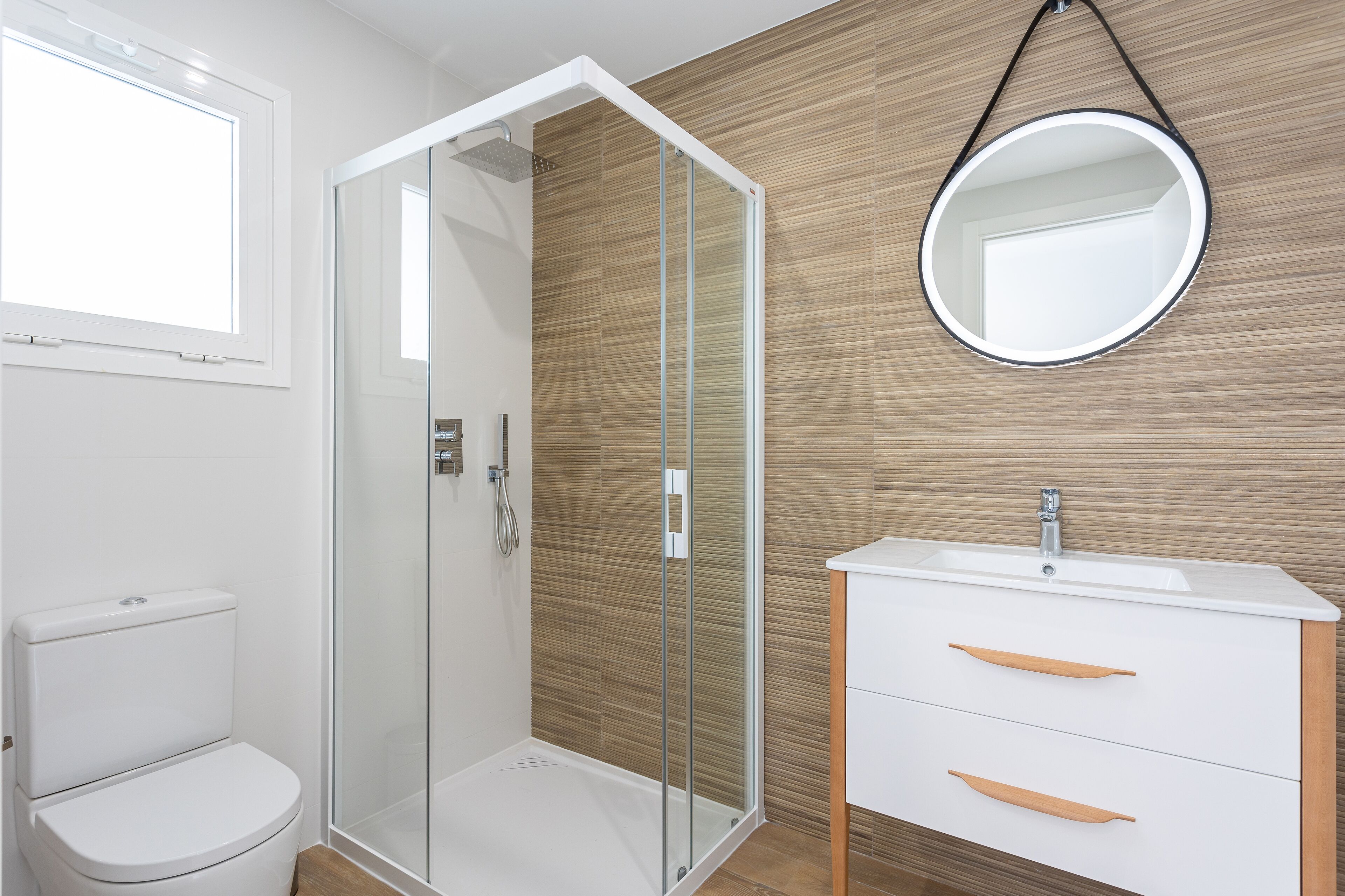 Une salle de bain moderne avec une douche à parois de verre, des toilettes blanches et un meuble-lavabo en bois avec un miroir.