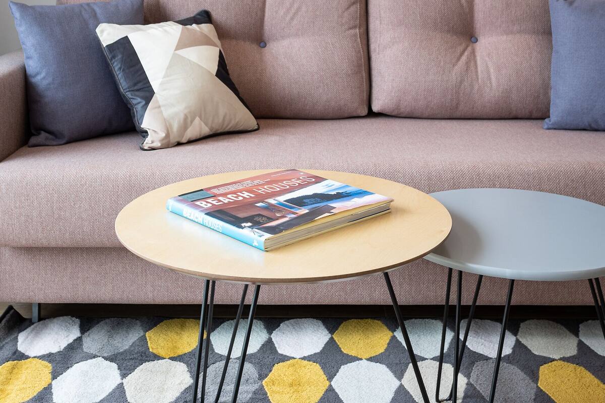 A living room with a sofa, two framed pictures on the wall, a coffee table with a book, and a patterned rug.