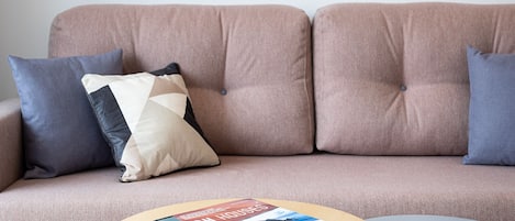 A living room with a sofa, two framed pictures on the wall, a coffee table with a book, and a patterned rug.