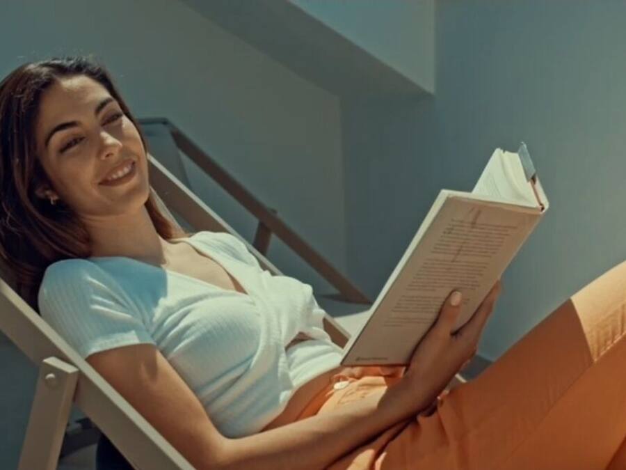 Una persona recostada en una tumbona leyendo un libro.