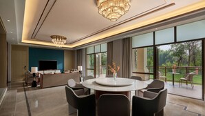 A modern living room with a large TV, comfortable seating, a dining table, and large windows offering a view of the outdoors.