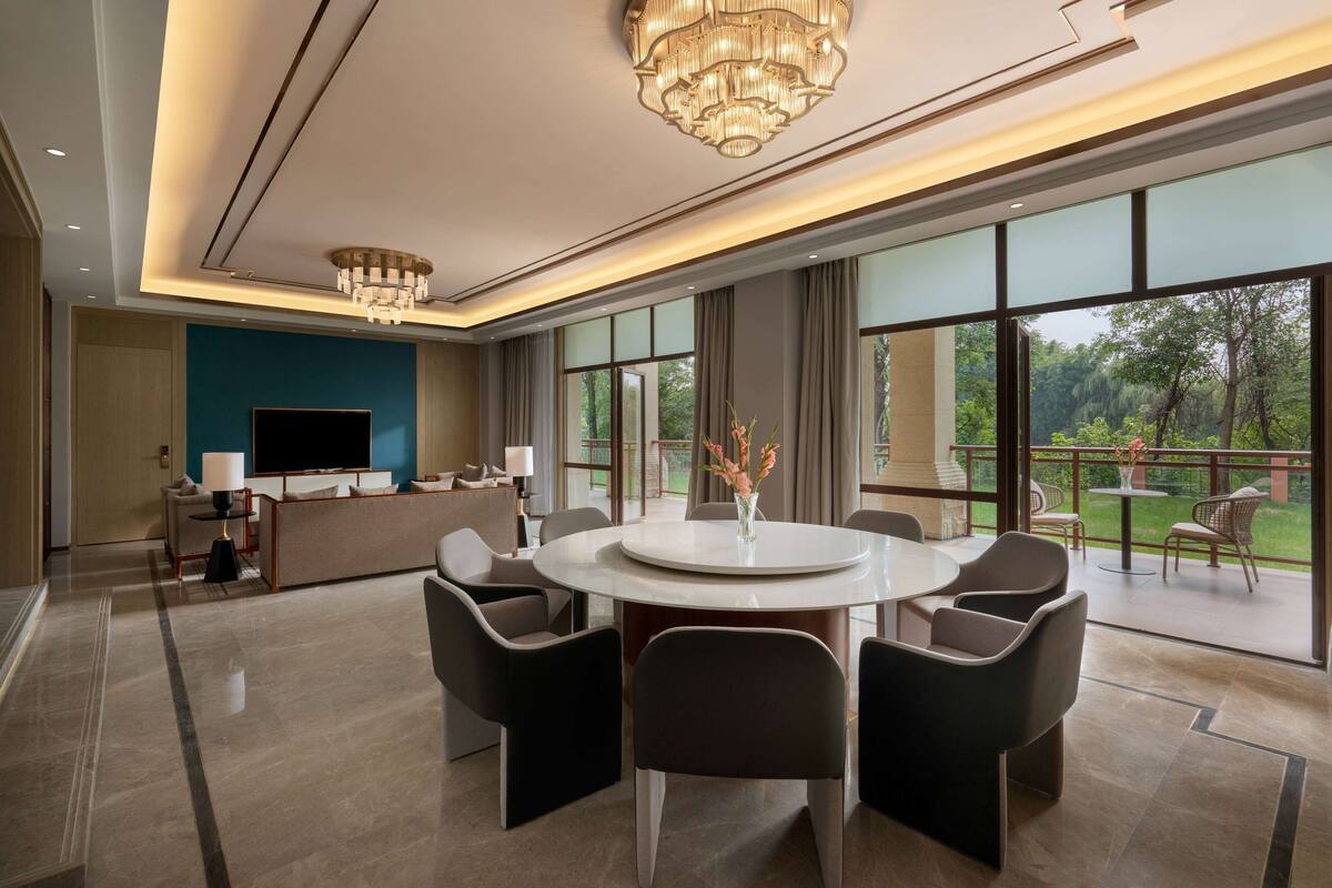 Een moderne woonkamer met een grote televisie, comfortabele zitplaatsen, een eettafel en grote ramen met uitzicht op de omgeving.