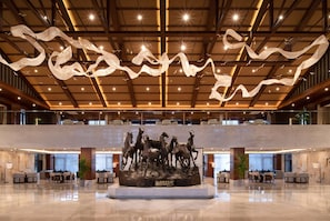 Un hall espacioso con una escultura central de caballos, techos altos con telas colgantes y un suelo de mármol pulido.
