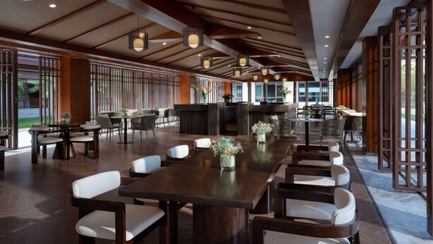 A spacious indoor area with wooden tables and chairs, a reception desk, and large windows allowing natural light.