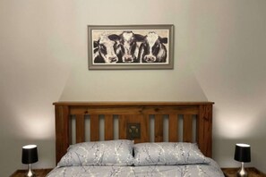 Un dormitorio con cabecera de madera, un cuadro enmarco con vacas y dos lámparas de noche.