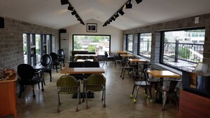 A spacious room with multiple tables and chairs, large windows offering views of the city, and a brick wall on one side. - Hwangsil Tourist Hotel (Jeonju)