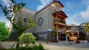 A traditional building with a large sign, a balcony, and a paved area with trees. - Hwangsil Tourist Hotel (Jeonju)