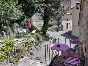A courtyard with a stone wall, a small table with a chair, and a red umbrella.