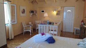 Un dormitorio acogedor con cama, dos sillas, una mesita y un escritorio. Se ve una puerta y una ventana con cortinas.