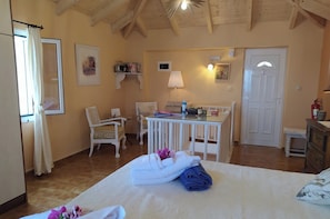 Une chambre confortable avec un lit, deux chaises, une petite table et un bureau. On y trouve une porte et une fenêtre avec des rideaux.