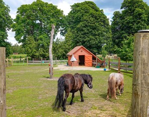A stable with two horses, surrounded by a fenced area and trees.