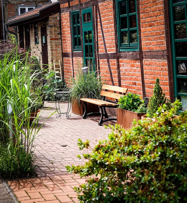 A brick building with green window frames, a wooden bench, and potted plants.