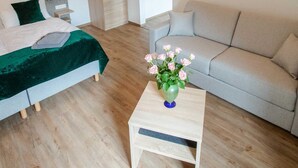 A bedroom with a bed, a sofa, a small table with a vase, and a wooden wardrobe.