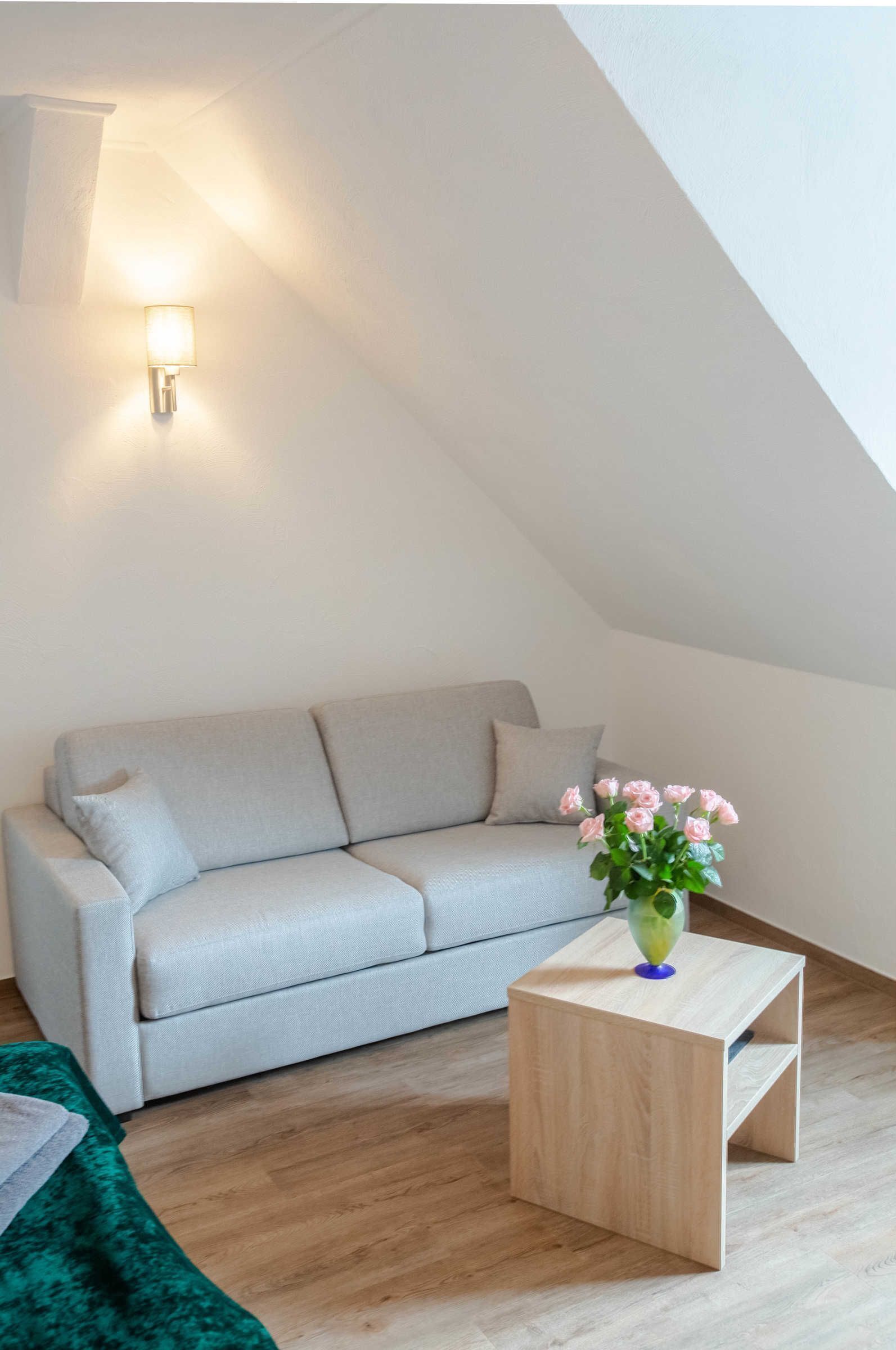 A modern living room with a light grey sofa, a wooden coffee table with a vase of flowers, and a wall-mounted light fixture.