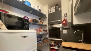 Ett kompakt kök med ett vitt kylskåp, en mikrovågsugn, en inbyggd ugn och en diskho.