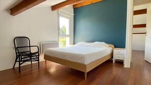 Un dormitorio con cama, una silla, una mesita de noche y una ventana.