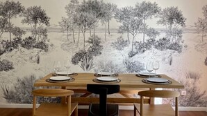 Un comedor con una mesa dispuesta para cuatro, sillas de madera y un mural de un paisaje en la pared.