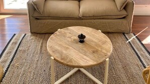 Una sala de estar con un sofá color beige, una mesa de centro redonda de madera y una lámpara de techo tejida.