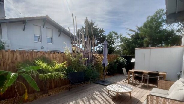 Una terraza de madera con mobiliario exterior, un edificio blanco y una valla de madera.