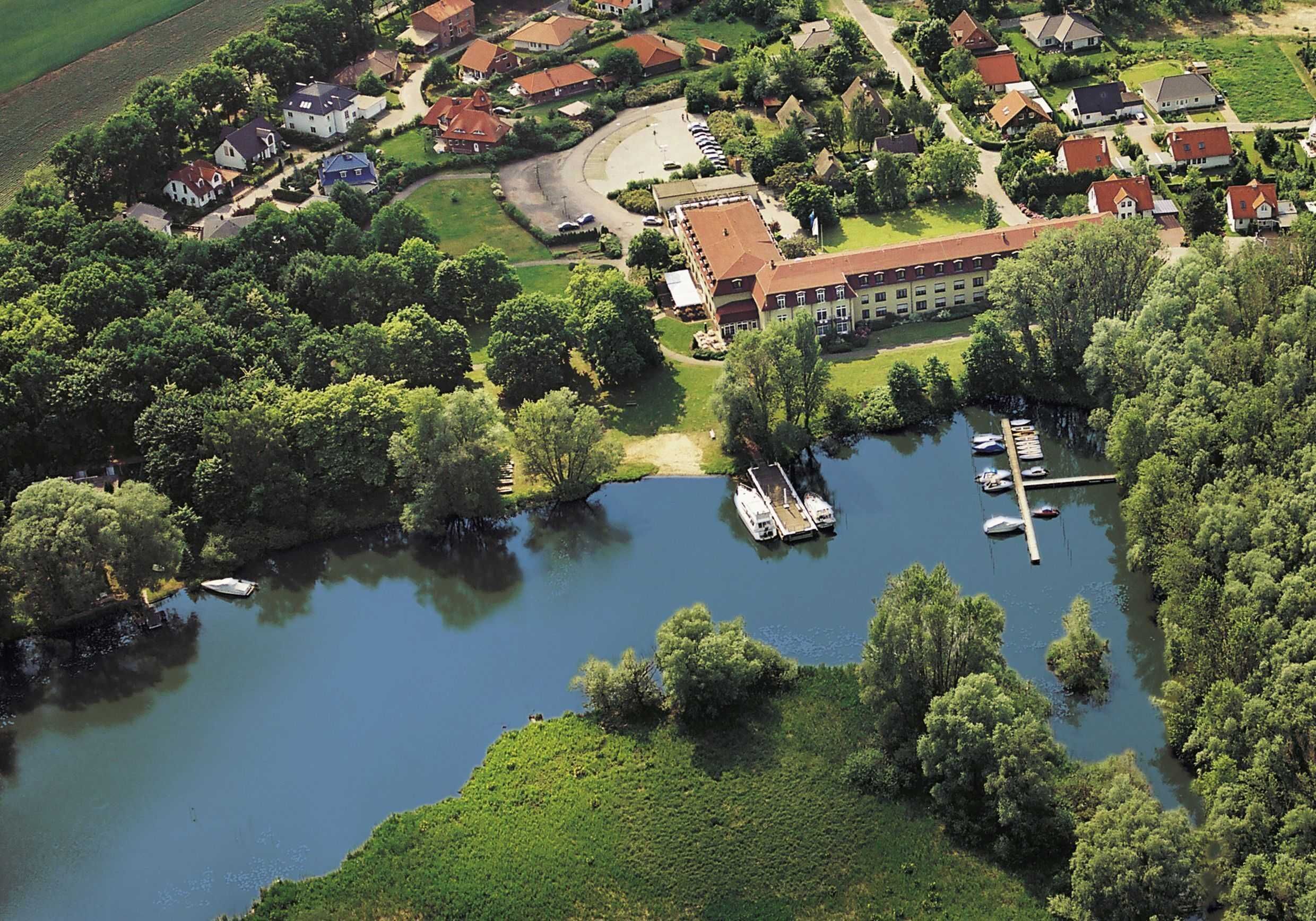 Eine Luftaufnahme eines Sees mit einem Grundstück, einem großen Gebäude, angestaubten Booten und umgebender Vegetation.