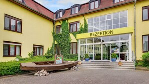A yellow building with a reception area, a boat sculpture, and steps leading to the entrance. - Standard double room - Seehotel Brandenburg. (Beetzsee)