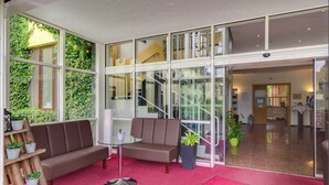 A modern interior with a red carpet, a brown sofa, a glass table, and a staircase leading to an upper level. - Standard double room - Seehotel Brandenburg. (Beetzsee)