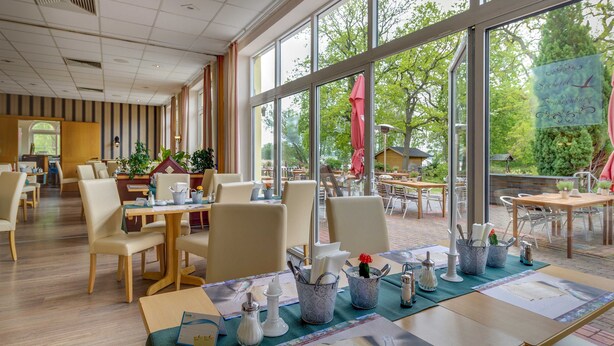 A restaurant with large windows, indoor seating, and a view of the outdoors. - Standard double room - Seehotel Brandenburg. (Beetzsee)