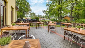 An outdoor patio with wooden tables and chairs, surrounded by a wooden fence and greenery. - Standard double room - Seehotel Brandenburg. (Beetzsee)