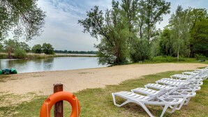 A lakeside area with white lounge chairs and an orange lifebuoy on a wooden post. - Standard double room - Seehotel Brandenburg. (Beetzsee)