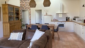 Una sala de estar acogedora con un sofá marrón, una mesa de comedor con sillas, una zona de cocina con microondas y estufa, y vigas de madera en el techo.