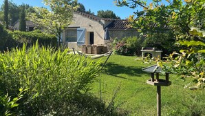 Una casa con techo de tejas, un jardín con una hamaca y un comedero para pájaros.